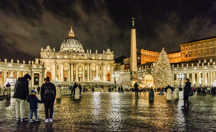 Nighttime view of people gathered in front of the Vatican, with special events taking place at St. Peter's Basilica.